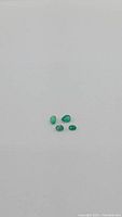 Four small natural emerald gemstones laid out on a neutral background showing their minimal size and green color.