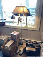 Full view of Baldwin brass floor lamp standing next to window with lampshade on and several boxes and items at base of lamp