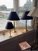 View of two large Baldwin brass table lamps and one smaller brass lamp with matching blue shades placed on a window sill