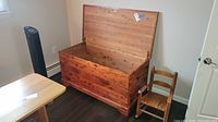 Open cedar chest with visible interior and push button lock on lid, next to small wooden child's rocking chair.