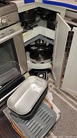 Cookware pots and pans stored in kitchen corner cabinet shelves including lids.