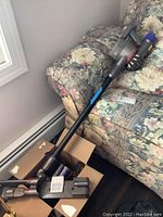 Multiple Dyson vacuum components including motor body, extension wand, floor head and wall mount in box on couch