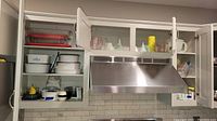 Kitchen cabinet with CorningWare dishes, Pyrex bowls and baking dishes, measuring cups, Polder kitchen scale, white juicer, funnels, and other kitchenware items