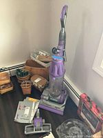Purple Dyson DC07 Animal upright vacuum next to baskets and instruction manuals on dark hardwood floor.