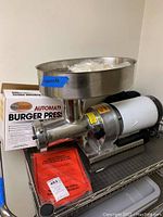 Stainless steel electric grinder with large hopper bowl mounted on base with electric motor and power cord