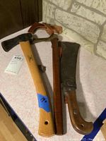 Two tools side by side: a hatchet with wooden handle and leather sheath, and a large machete with wood handle and metal sheath.