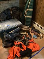 Photo showing the clothing items (orange vest, camo boots), holsters, firearms cases, and accessories arranged on the floor with the ScentLok bin behind.