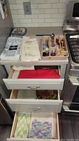 View of countertops and three drawers showing towels, hot pads, bottle openers in a tray