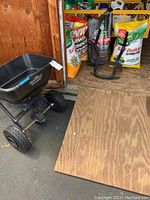 Full view of the broadcast spreader, wheelbarrow frame and lawn treatment bags placed in a wooden shed area.