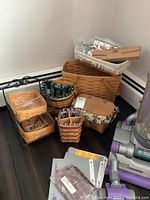 Overview of all 7 baskets and accessories arranged on dark hardwood floor, includes baskets with fabric liners and a metal basket holder.