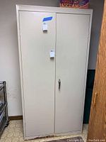 Front view of closed, double door metal cabinet showing standard handle and some surface imperfections