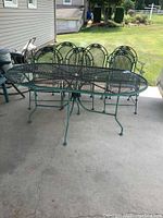 Wide angle photo showing the entire patio set including the oval table and six chairs arranged outdoors on a concrete patio.
