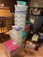 Stack of 20 varying sized plastic storage containers with lids in a room with wooden floor and furniture.