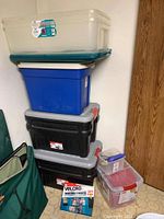 Stack of various plastic storage containers including two large Rubbermaid Action Packers and several clear and colored lid bins, plus a box of Velcro in front.