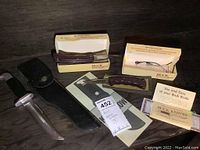 Overview of all three knives including the Bowie knife with sheath and two folding knives in original Buck boxes with instruction pamphlets.