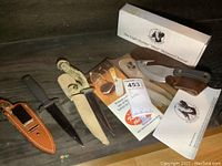 Overall view of the three knives, one with box, sheaths, and paperwork visible