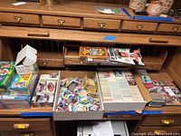 Wide shot showing multiple boxes and loose sports cards on a wooden desk with divided compartments. Boxes include various card sets and loose cards in small piles and boxes.