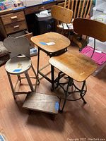 Overall view of two tall stools with wooden seats and backs, metal frames, and one smaller wooden foot stool on floor.