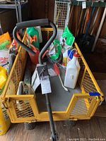 Yellow metal garden wagon loaded with various lawn and garden products including a blower, watering can, and yard chemicals.