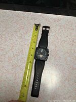 Full view of watch laid flat beside measuring tape showing overall length and strap