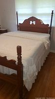 Full view of the antique full-size bed with bedding covering mattress, showing spool posts and carved headboard.