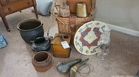 Wide shot showing grouped antique and primitive decor items including woven basket lid, oil lamp, powder horns, metal and cast iron pots, wooden bucket, hand-crank coffee grinder, and wicker basket.