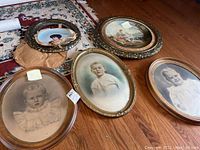 Photo of all five oval framed portraits and art arranged on wooden floor showing full lot including the damaged frame