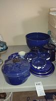 Blue ceramics including large enamel pot with lid, three Roseville mixing bowls with white design, small bowls and plates, arranged on table.