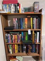 Photo of wooden bookshelf showing multiple fiction books including Harry Potter series, various VHS tapes, and some DVDs