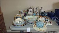 Full view of table displaying over 50 pieces of china including teapots, plates, pitchers, and bowls in varied patterns and colors