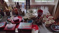 Overview of assorted Christmas ornaments, decor, mugs, glasses, and boxes on a surface near window light.
