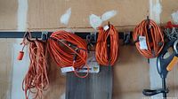 Four orange extension cords hanging on hooks against a wall