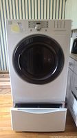 Front view of white Kenmore front loading dryer with circular black door and pedestal drawer open at bottom