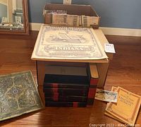 Two boxes containing stacked hardcover books, some with red and black bindings identified as The Harvard Classics. Includes a map of Indiana and additional books piled on the side.