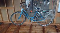 Full side view of blue vintage girl's Schwinn bicycle with two rear wire baskets and white padded backrest seat, hanging from ceiling.