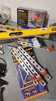 Photo showing yellow Craftsman level, metal frame clamps, and boxed Ryobi sander on concrete floor.