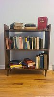 Front view of the small wood bookcase filled with various vintage hardcover books showing aging and damage.