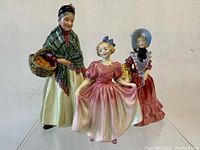Front view showing three porcelain Royal Doulton figurines - The Orange Lady, Sweeting, Lady Betty