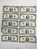 15 U.S. two dollar bills laid in rows showing front sides for condition assessment.