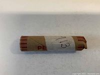 Photo of the sealed cylindrical paper-roll containing unsearched 1913 wheat pennies, handwritten label on white paper reading '1913', roll wrapper in brown and red stripes.