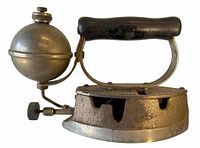 Side view of antique self heating iron showing metal body, round fuel tank attached on left side, and black handle