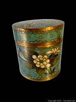 Front and side view of the round cloisonné box showing blue enamel with floral decoration and gold trim.