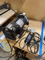 Overall view of bench grinder showing grinding wheels and handheld sander/grinder tool on wooden surface