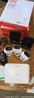 View of four white Arlo security cameras, two black speakers, printer paper stacked behind, and white Arlo base station at bottom