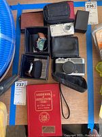 Overview photo showing two Oshen watches in boxes, Sony Cyber-shot camera, Canon camera with case, and a red coin guide book.