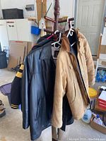 Four coats hung on a wooden rack in a garage-like space, showing various colors and materials