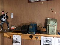 Photo of shelf showing from left to right: battery operated Elvis Presley doll with guitar and microphone, unassociated mug, vintage metal banks including Universal and Uncle Sam three coin register banks, vintage bell, licorice wafers container, and Gloucester business directory.