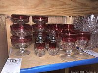 Set of red tinted glass goblets, dessert glasses and cut glass salt and pepper shakers displayed on a wooden shelf.