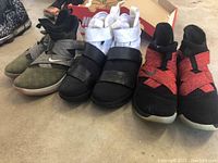 Three pairs of Nike Lebron sneakers positioned side by side on concrete floor, showing color and strap details.