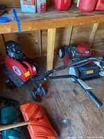 Full view of the RedOx rototiller positioned on wooden floor with gardening tools nearby showing device length and handlebar.